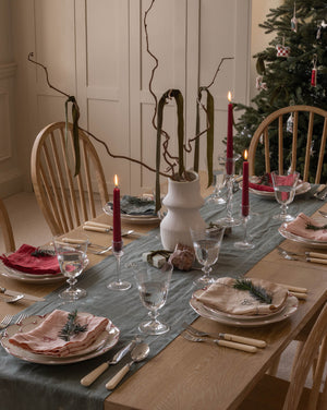 Dining table set for a meal with Christmas decorations, including a tree and candles.
