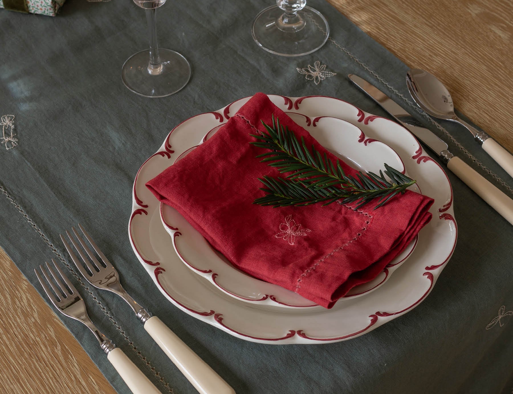 Dining table setting with red napkin, white plate, and silverware on a dark green tablecloth.