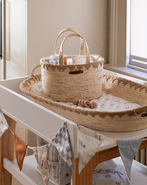 Woven basket and tray on a changing table with baby items in a nursery.
