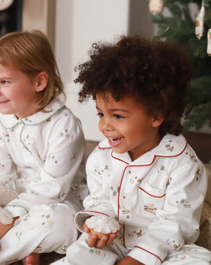 Two children in white pajamas with red trim sitting next to a Christmas tree.
