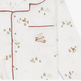 Close-up of a white long-sleeve pajama top with red piping and a small chest pocket featuring a printed ski-and-stove motif, shown against a white background.