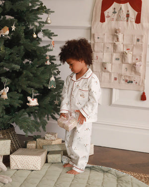 Child in pajamas standing next to a decorated Christmas tree with presents underneath.