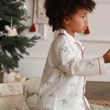 Child in pajamas standing in a room with a Christmas tree and presents.