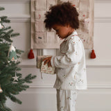 Child in pajamas opening a gift near a Christmas tree with an advent calendar in the background.