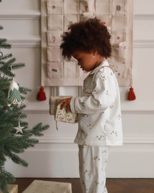 Child in pajamas opening a gift near a Christmas tree with an advent calendar in the background.