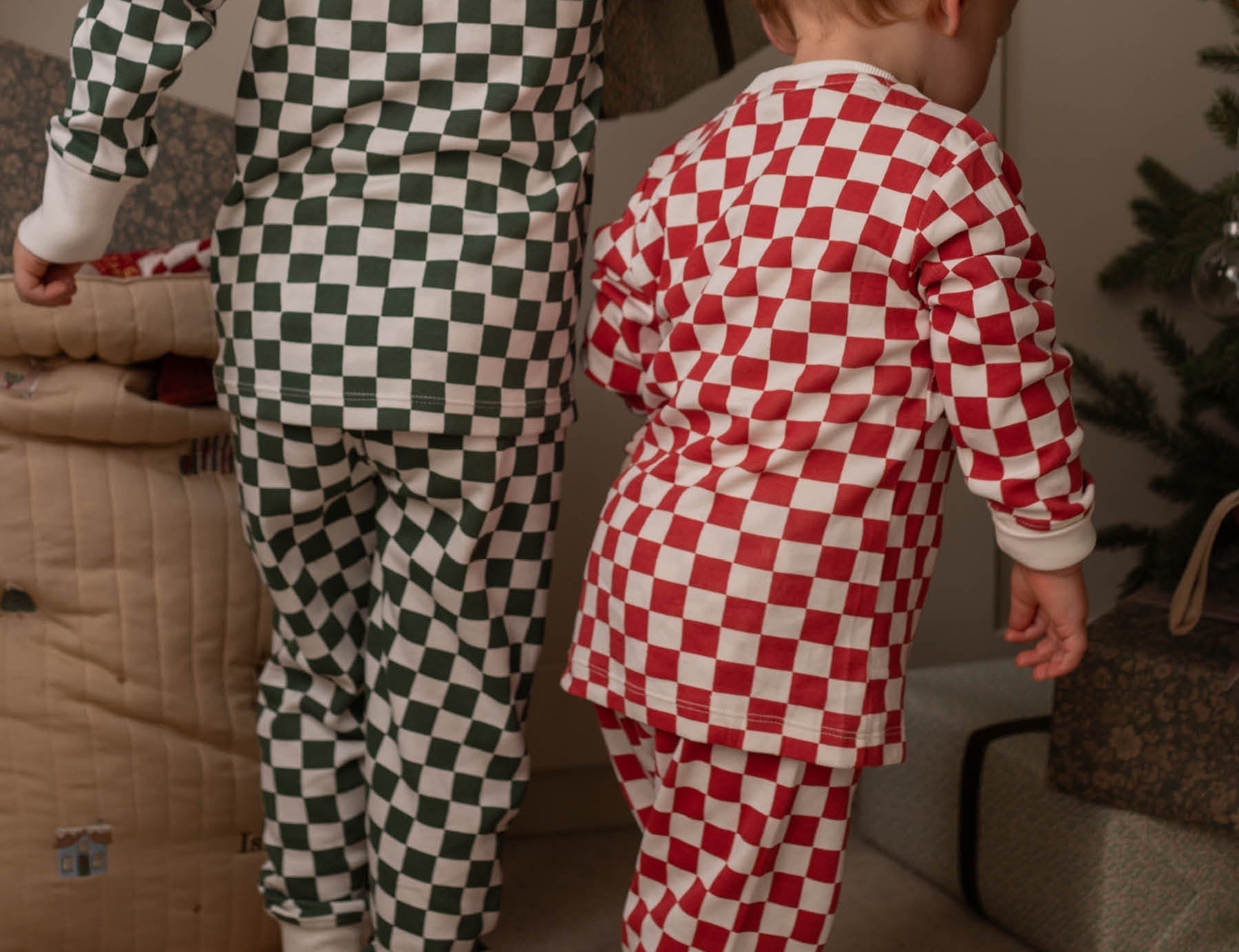 Two children wearing checkered pajamas standing in a room with a Christmas tree.