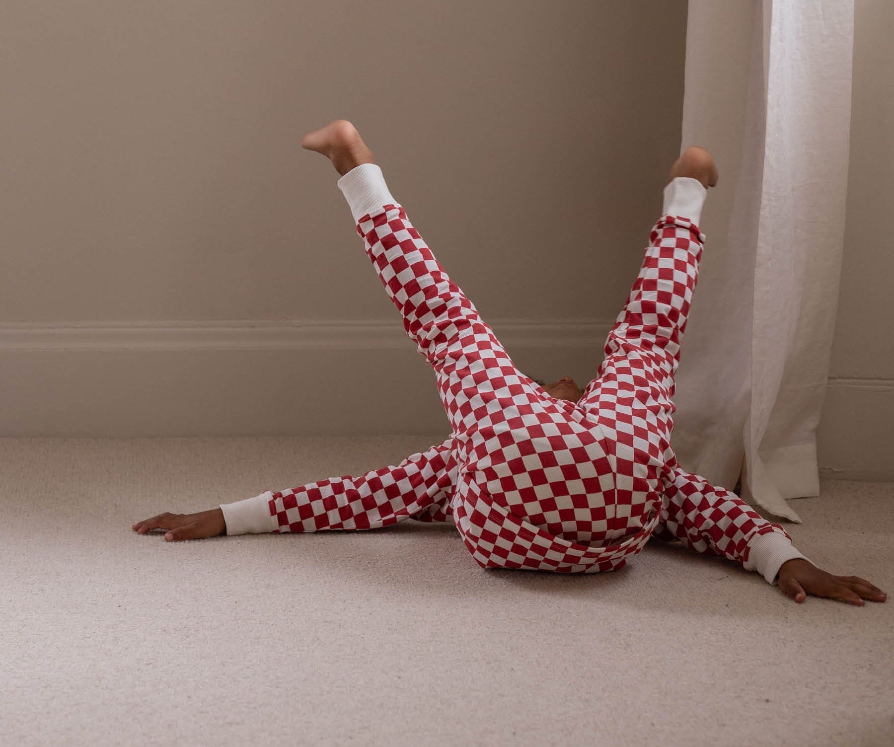 Person wearing red and white checkered pajamas lying on a beige carpeted floor.
