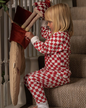 Child in red and white checkered outfit playing with a large teddy bear on a staircase.