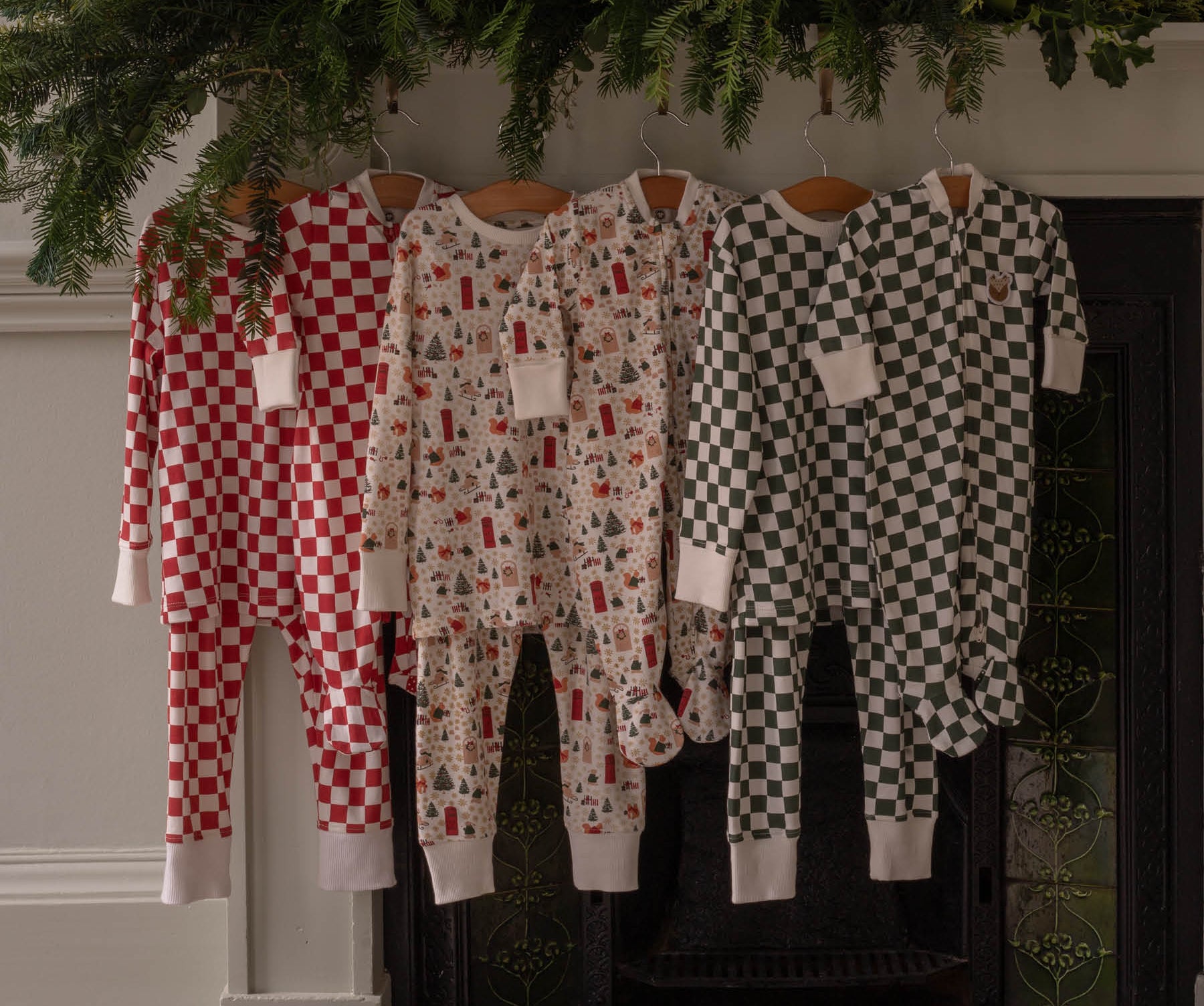 Three children's pajamas hanging on a fireplace mantle with Christmas decorations.