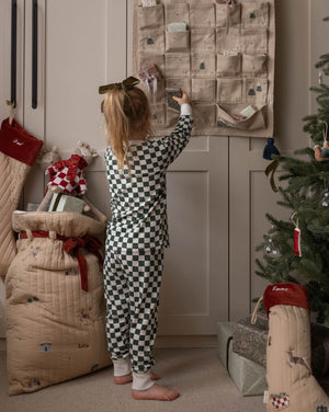 Child in pajamas reaching for a Christmas advent calendar next to a decorated tree and presents.