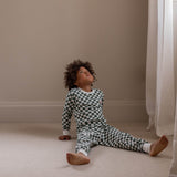 Child wearing a black and white checkered outfit sitting on the floor in a room with beige walls and white curtains.
