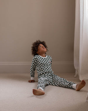 Child wearing a black and white checkered outfit sitting on the floor in a room with beige walls and white curtains.