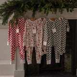 Three children's pajamas hanging on a fireplace mantle with Christmas decorations.