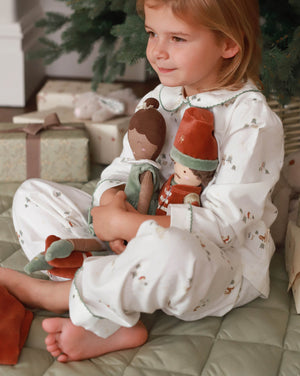 Child in pajamas holding a plush toy in a festive setting with presents and a Christmas tree.