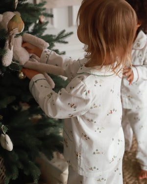 Child in pajamas decorating a Christmas tree with a teddy bear ornament.