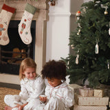 Two children in pajamas sitting by a Christmas tree and fireplace.