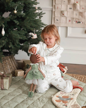 Child in pajamas playing with a doll next to a decorated Christmas tree.