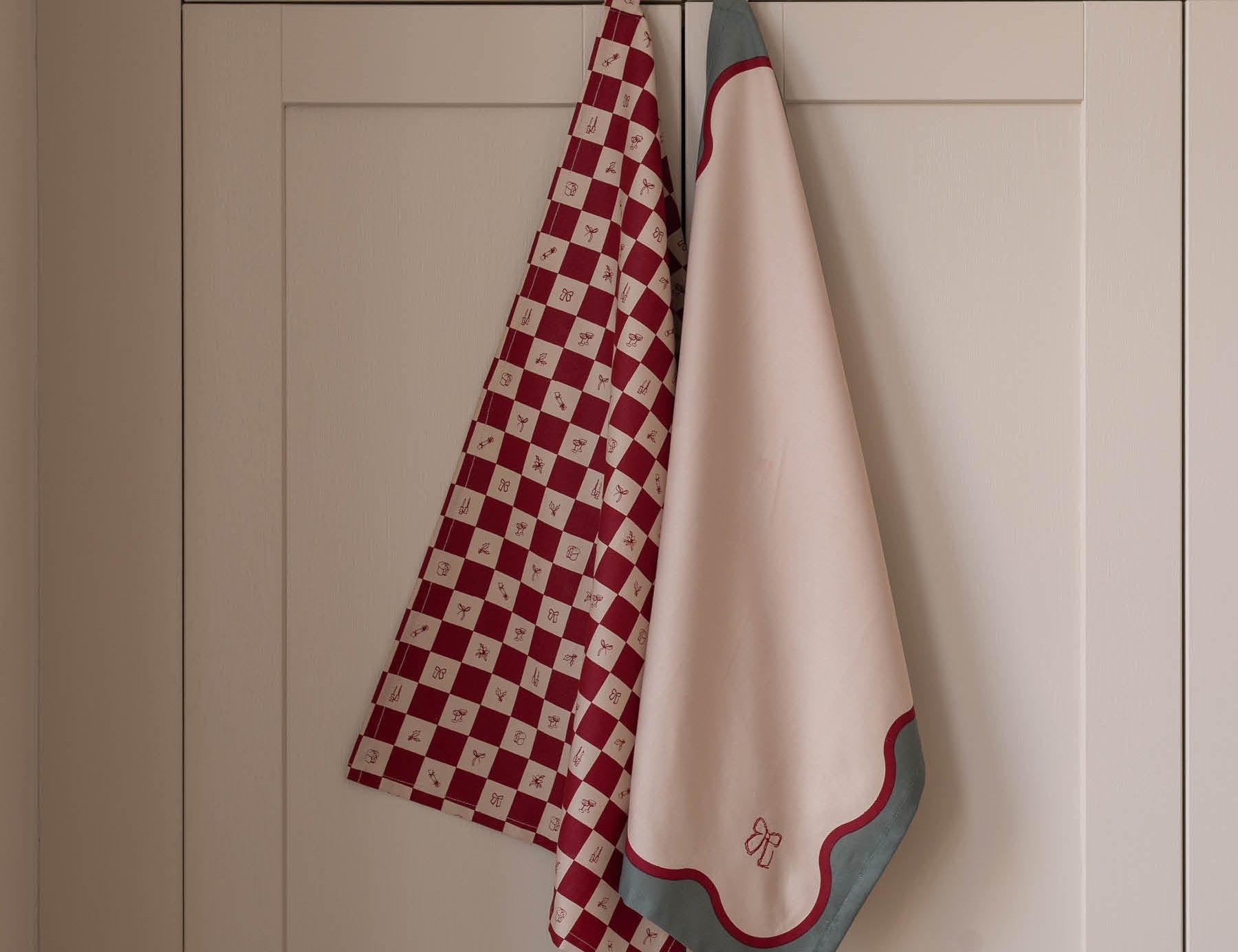 Two towels, one red and white checkered and one beige with a red border, hanging on a rack against a beige wall.
