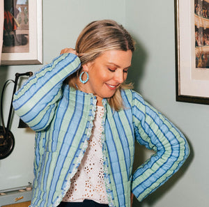 Woman wearing a blue striped jacket in a room with framed pictures on the wall.