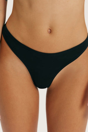 A close-up of a model wearing a solid black bikini bottom against a clean, off-white background.