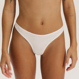 A close-up of a model wearing a white low-rise bikini bottom against a light beige studio background.
