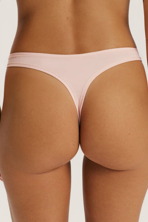 Rear view of a model wearing a light pink thong-style underwear bottom against a plain light gray studio background.
