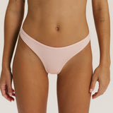 A close-up of a model wearing a light blush pink bikini bottom against a plain light background.