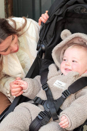 ALF Eco Pramsuit in beige worn by a smiling baby in a pushchair while a woman crouches beside them