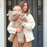Alf Eco Pramsuit Beige on a baby held upright against a smiling woman, showing the footed legs and bear-ear hood