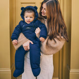 Anders Eco Snowsuit in navy worn by a baby held on the hip of a woman standing in front of a yellow door