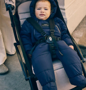 Anders Eco Snowsuit in navy worn by a baby with hood up, strapped into a pushchair seat
