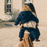 Anders Eco Snowsuit Navy worn by a toddler being carried on a woman's hip, seen from behind outdoors