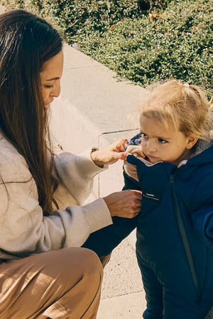 Anders Eco Snowsuit Navy on a toddler outdoors while a woman adjusts the front of the suit