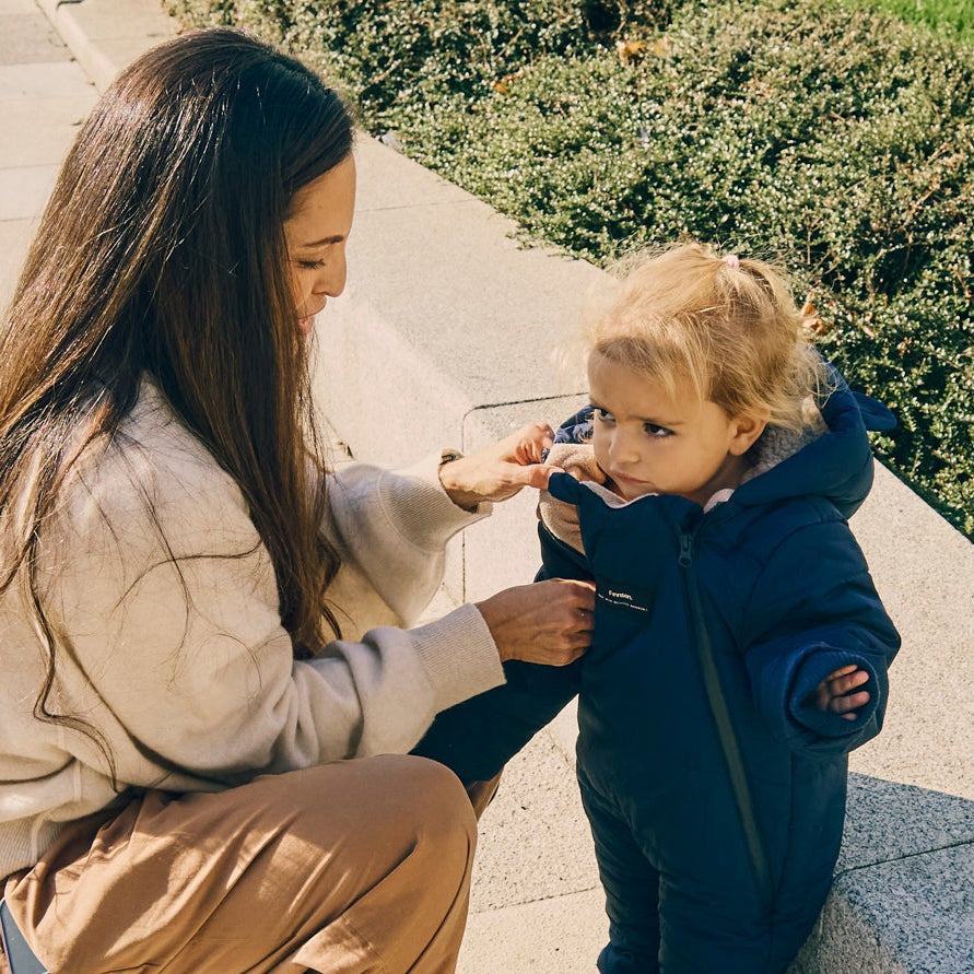 Anders Eco Snowsuit Navy on a toddler outdoors while a woman adjusts the front of the suit