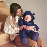 Anders Eco Snowsuit in navy on a baby sitting on a woman's lap on the stairs, spotted soles of the feet visible