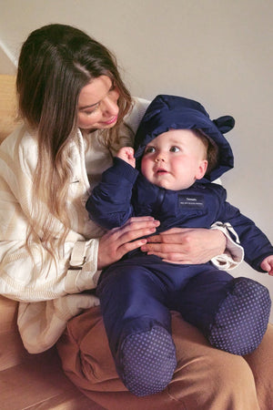 Anders Eco Snowsuit in navy on a baby sitting on a woman's lap on the stairs, spotted soles of the feet visible