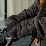 Astrid Eco Stroller Mittens Black, close-up of an adult wearing them over a pram handlebar, with Finnson label visible