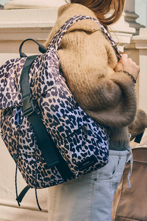 Elise Eco Changing Backpack Leopard worn on one shoulder by a woman standing beside a pram