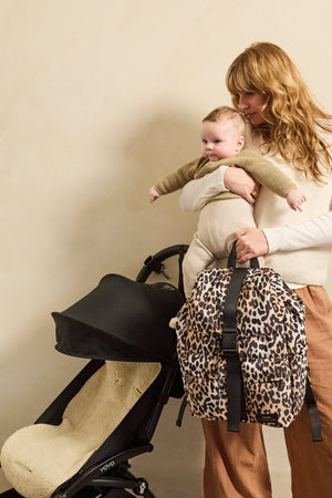 Elise Eco Changing Backpack Leopard held by a woman carrying a baby, next to a black pushchair