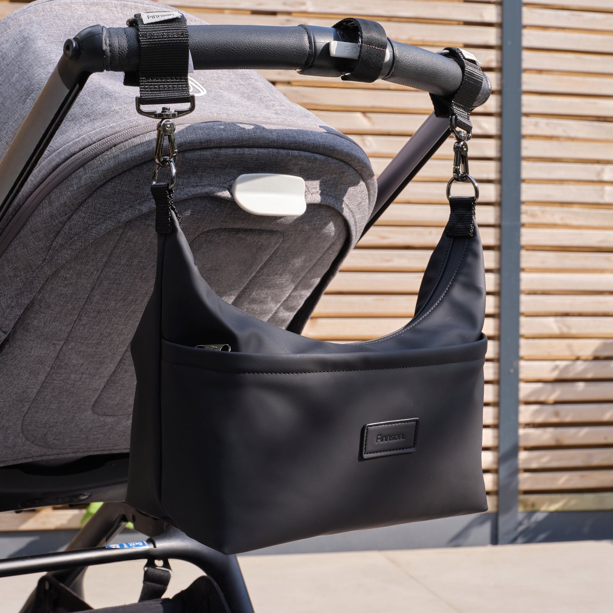 Fia Eco Stroller Organiser Black hanging from a pushchair handlebar by its two stroller clips
