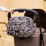 Freya stroller organiser in Leopard clipped to a stroller handle, with side pockets and front zip pocket