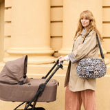 Woman in a trench coat pushing a pram with the Freya stroller organiser in Leopard over her shoulder