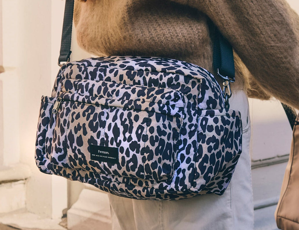 Freya stroller organiser in Leopard worn crossbody over a brown knit jumper