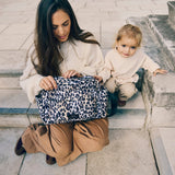 Woman opening the Freya stroller organiser in Leopard on her lap while a toddler sits beside her on stone steps