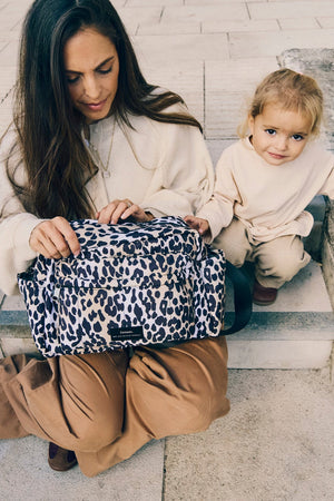 Woman opening the Freya stroller organiser in Leopard on her lap while a toddler sits beside her on stone steps