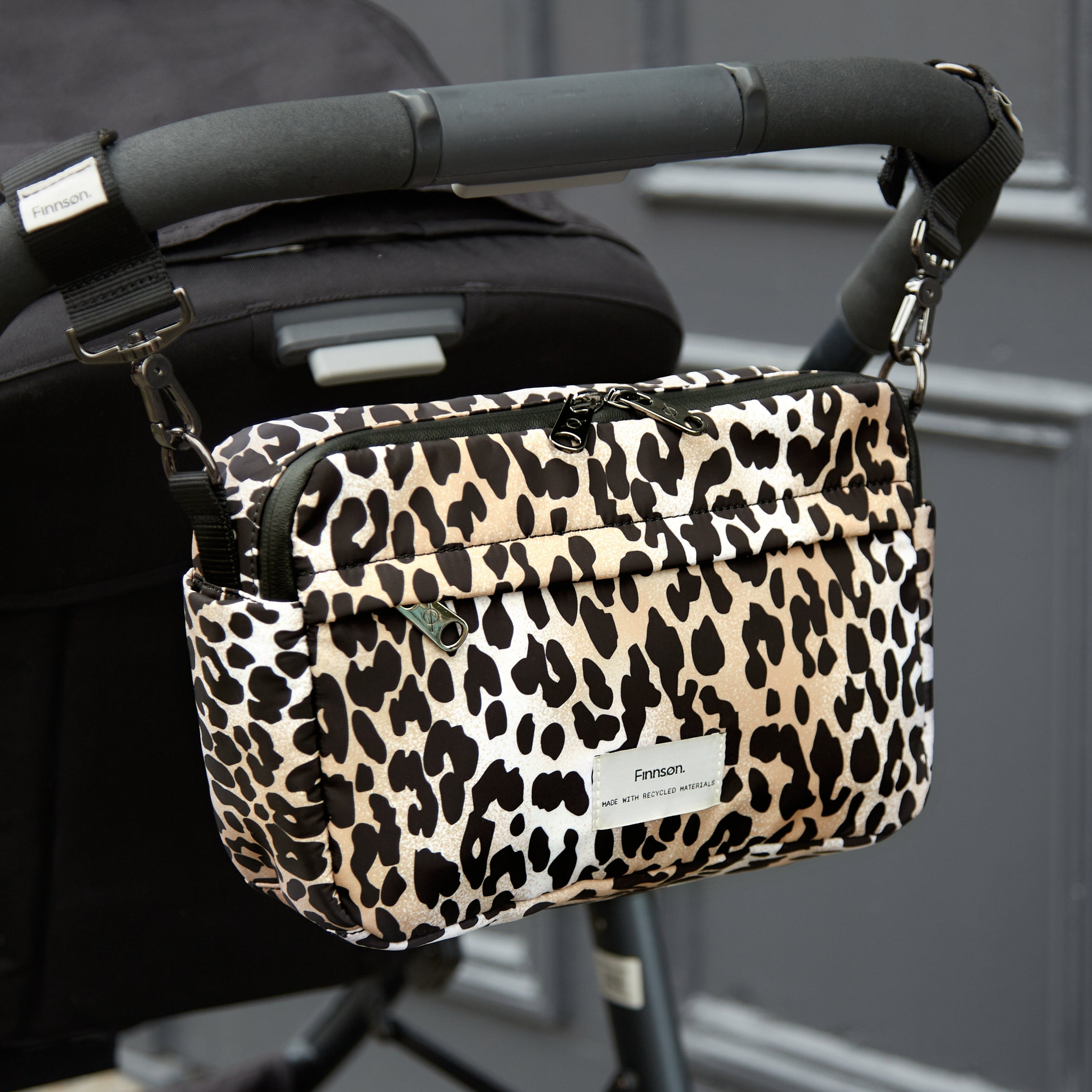 Frida Eco Stroller Organiser Leopard attached to a pushchair handlebar by its stroller clips, seen from the front