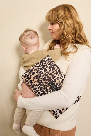 Oslo Eco Travel Changing Mat in Leopard worn across the body by a woman holding a baby against her shoulder
