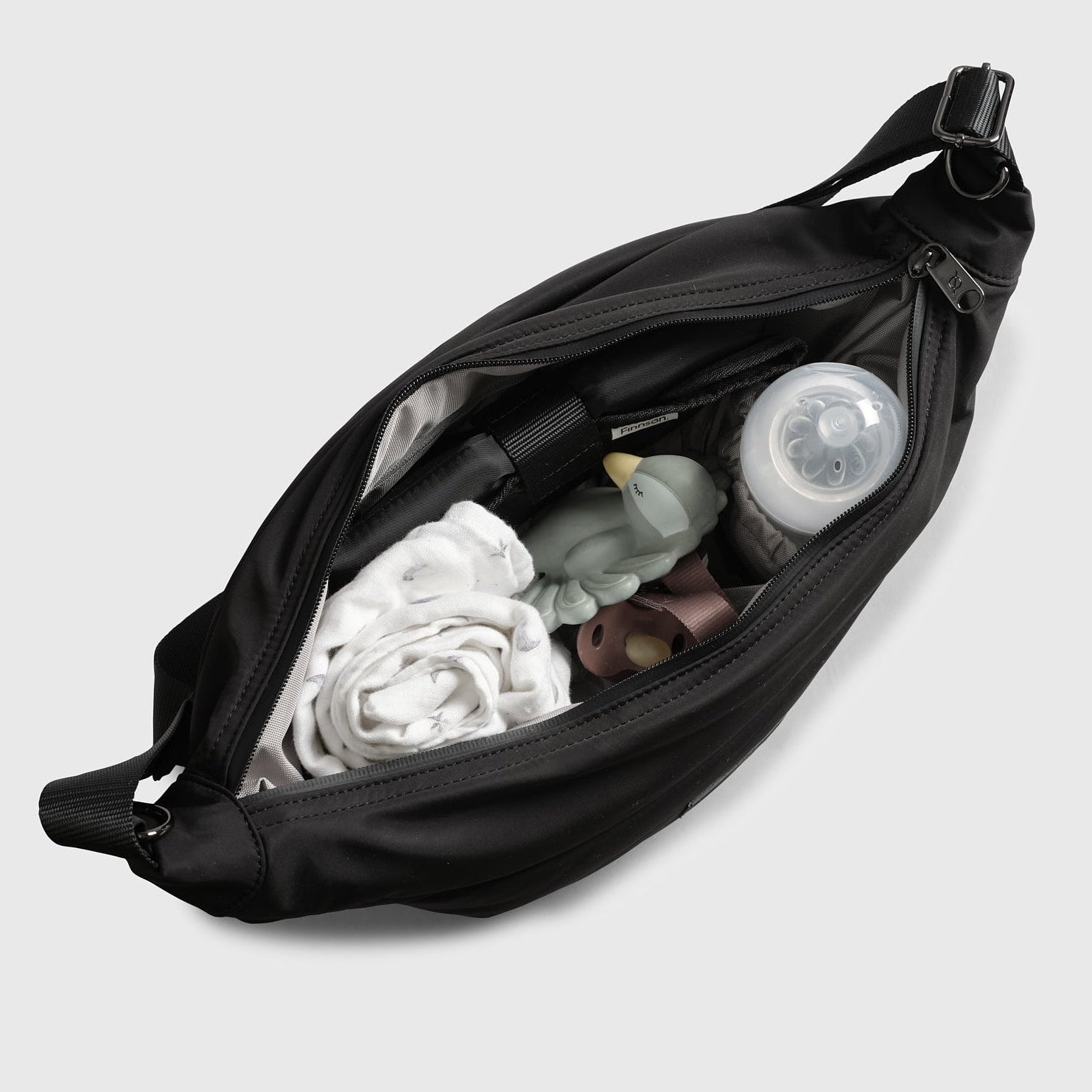 Osma Eco Stroller Organiser Black unzipped from above, holding a muslin, baby bottle, teether and dummy