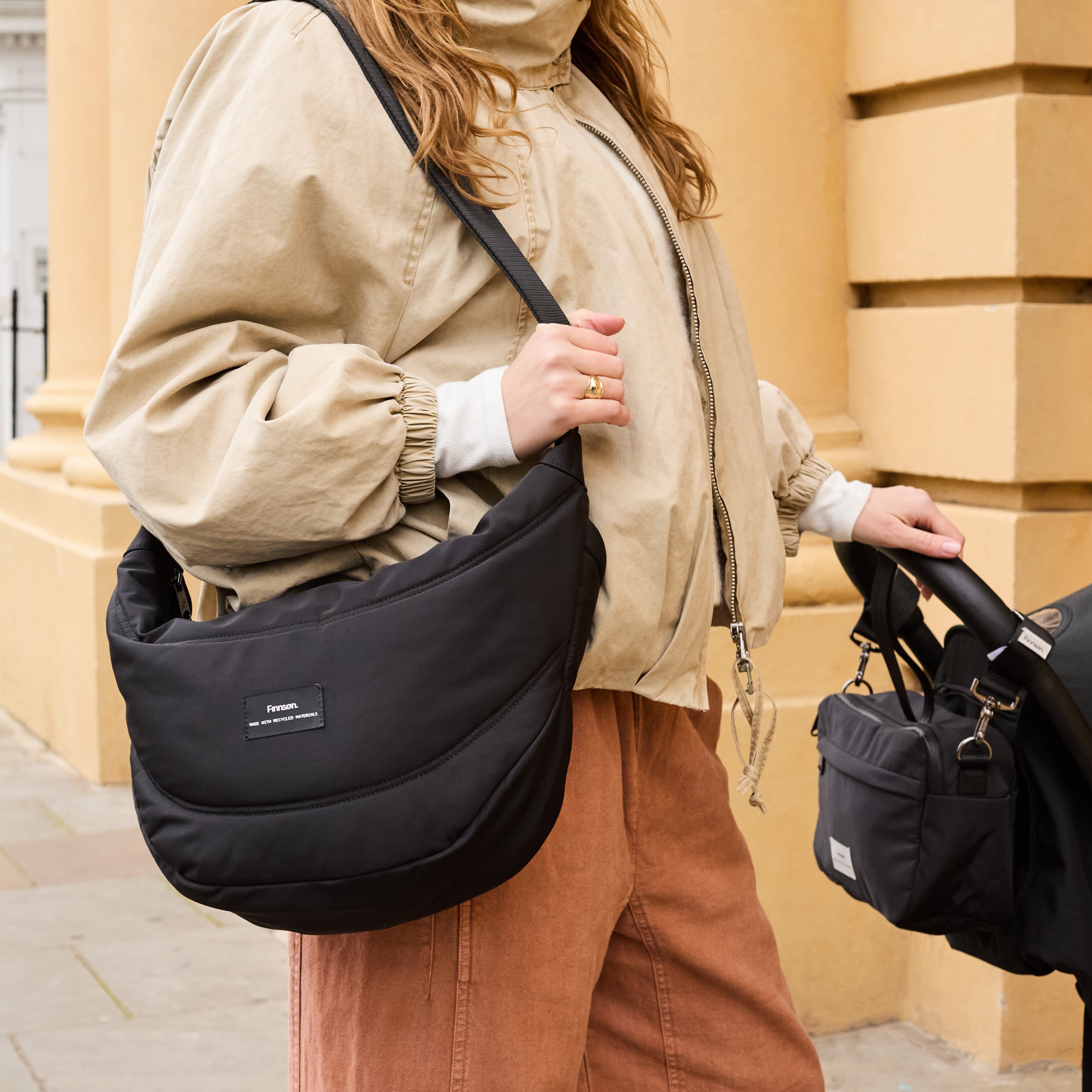 Osma Eco Stroller Organiser Black worn across the body by a woman with one hand on a pram handle