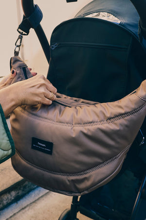Osma stroller organiser in Mocha clipped to a stroller handle while a hand reaches into the top zip